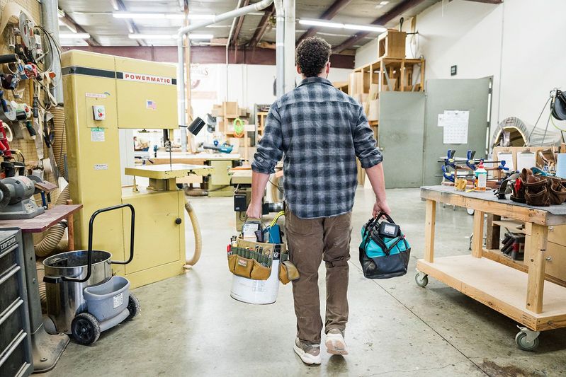 man entering wood working shop with 2 bags of tools