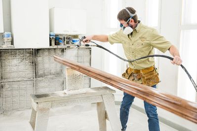 man spray staining wood in the paint room of the workshop